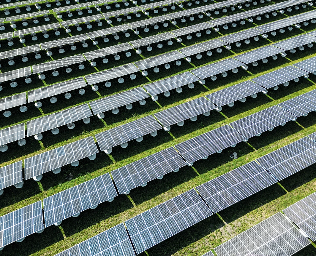 Zu sehen ist ein Ausschnitt der riesigen Photovoltaik Anlage in Lenzing. Zwischen den einzelnen Reihen der Photovoltaikpanele sind grüne Wiesenstreifen sichtbar.